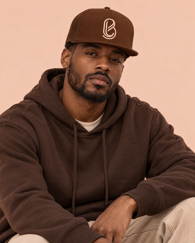 Bledlard Slapback Cap in chocolate with peach embroidered B, worn with a brown hoodie